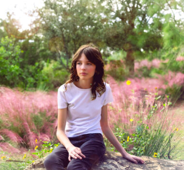girl sitting on a rock with pink grass behind her